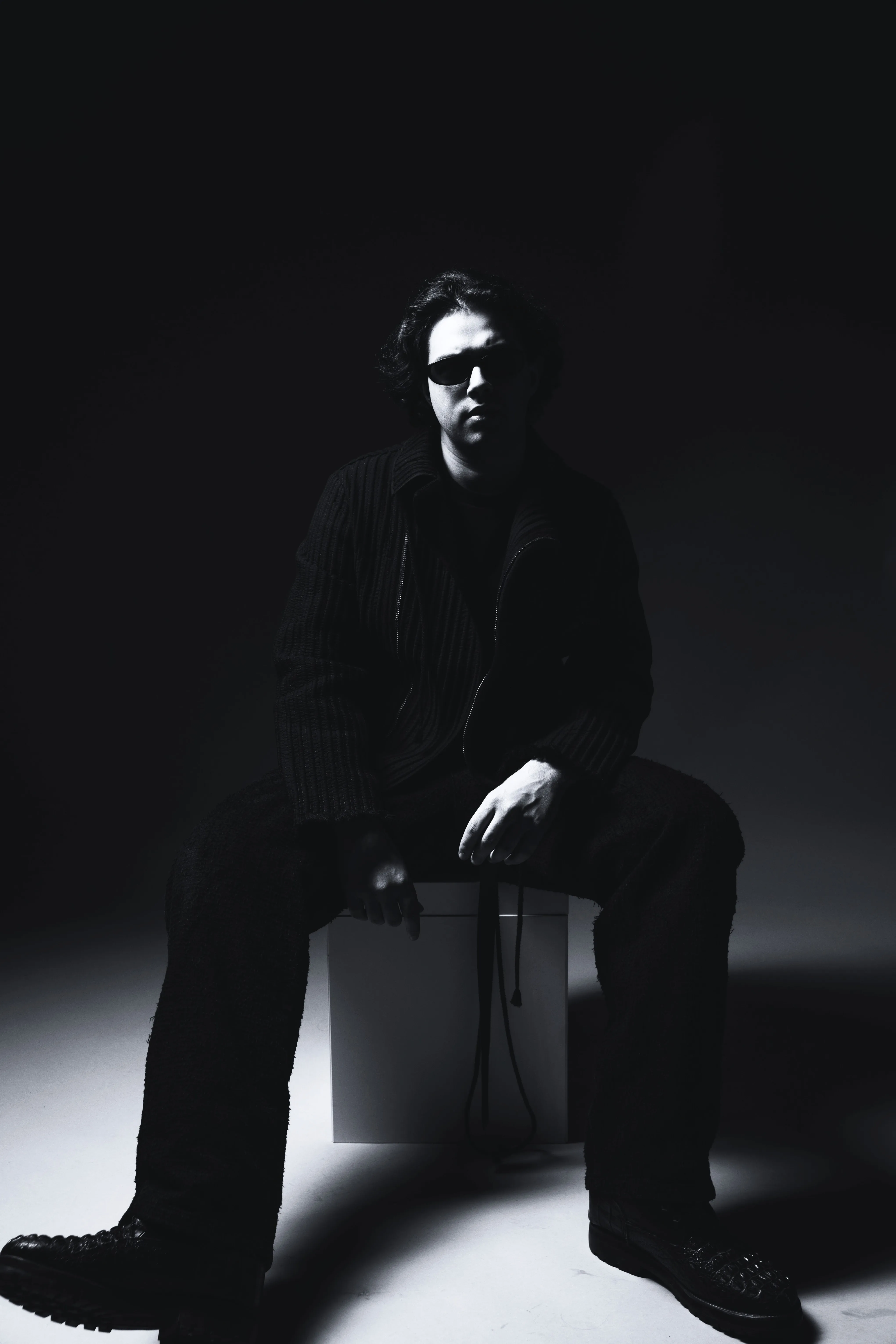 AMANN seated in a black-and-white studio portrait